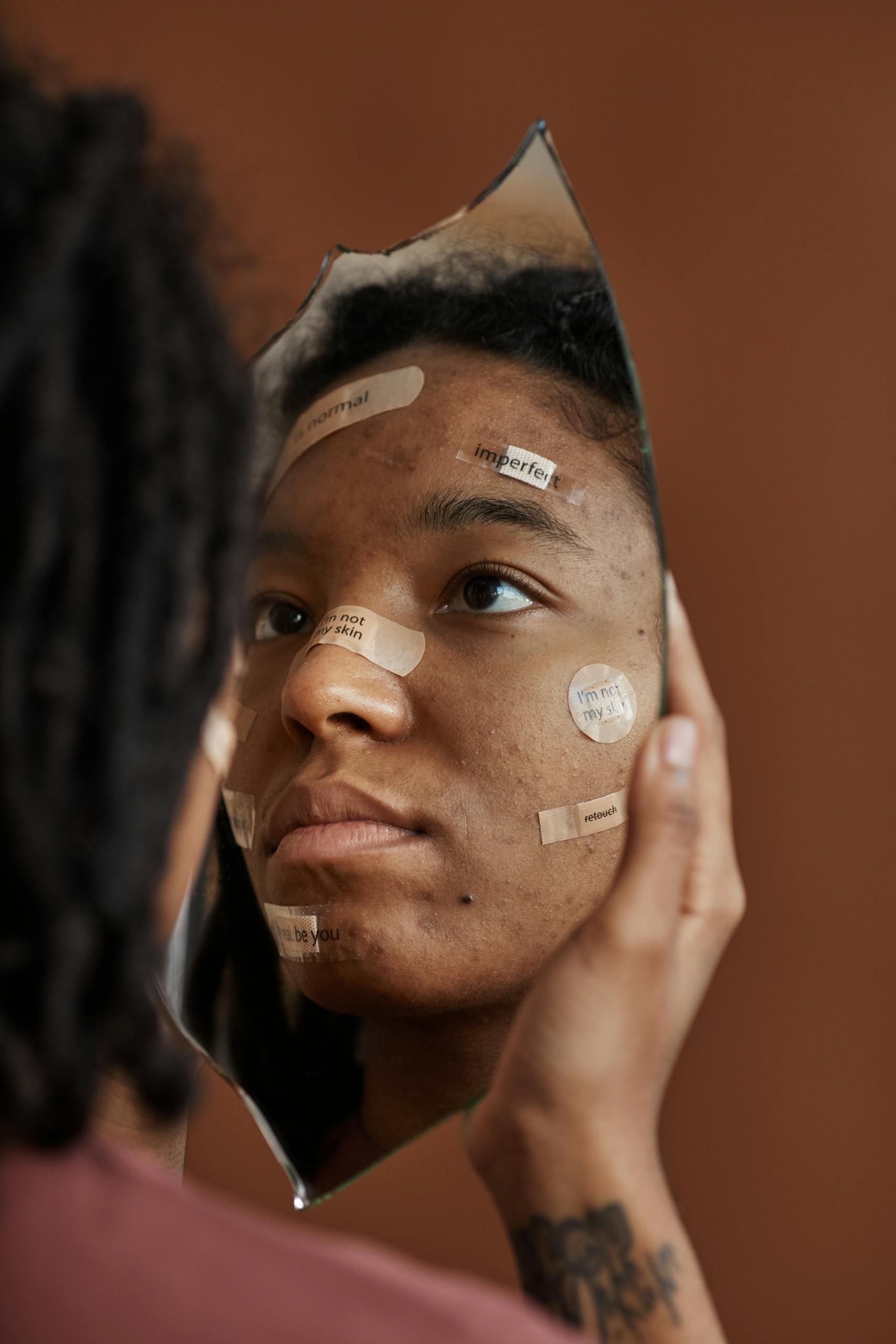 A Woman with Band Aids on Face Looking in a Broken Mirror